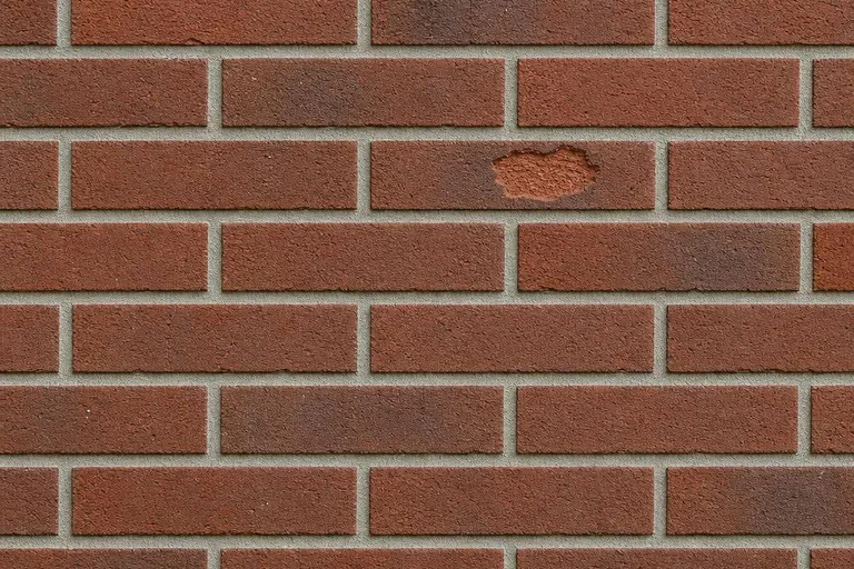 Two areas of restrained face spalling in an otherwise aligned red brick residential wall