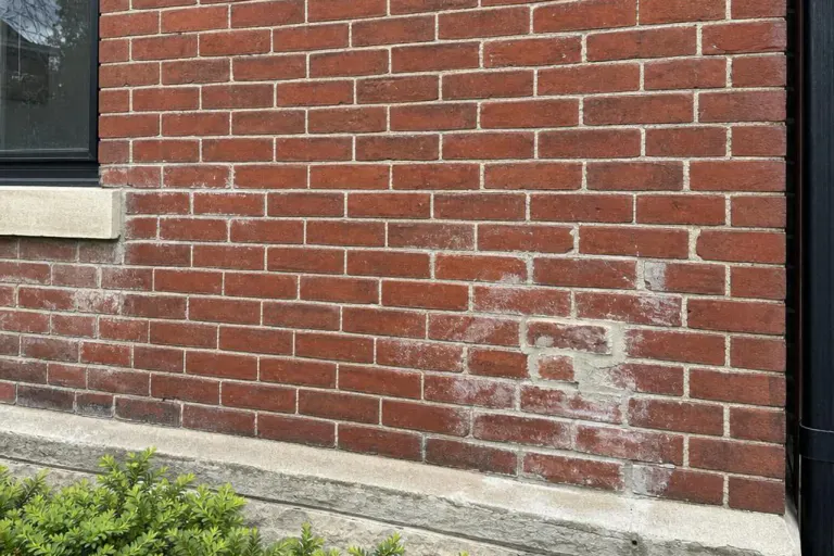 Weathered brick wall with efflorescence, worn mortar joints, and an incompatible patch repair