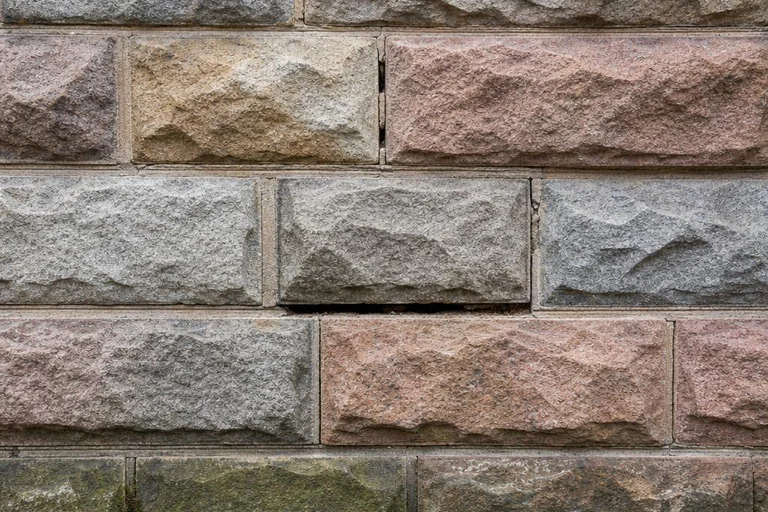Rock-faced stone foundation with eroded mortar joints, one open bed joint, and moss near grade