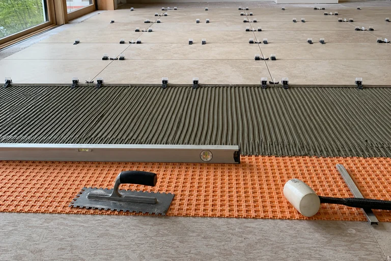 Porcelain floor installation with uncoupling membrane, directional thinset, leveling clips, reference lines, level, mallet, and trowels