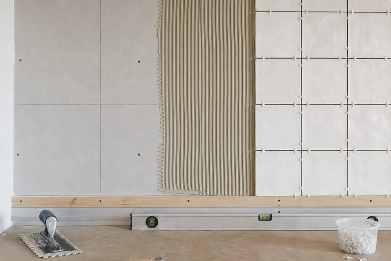 Backsplash installation with prepared substrate, directional thinset ridges, ledger, spacers, reference lines, and hand tools